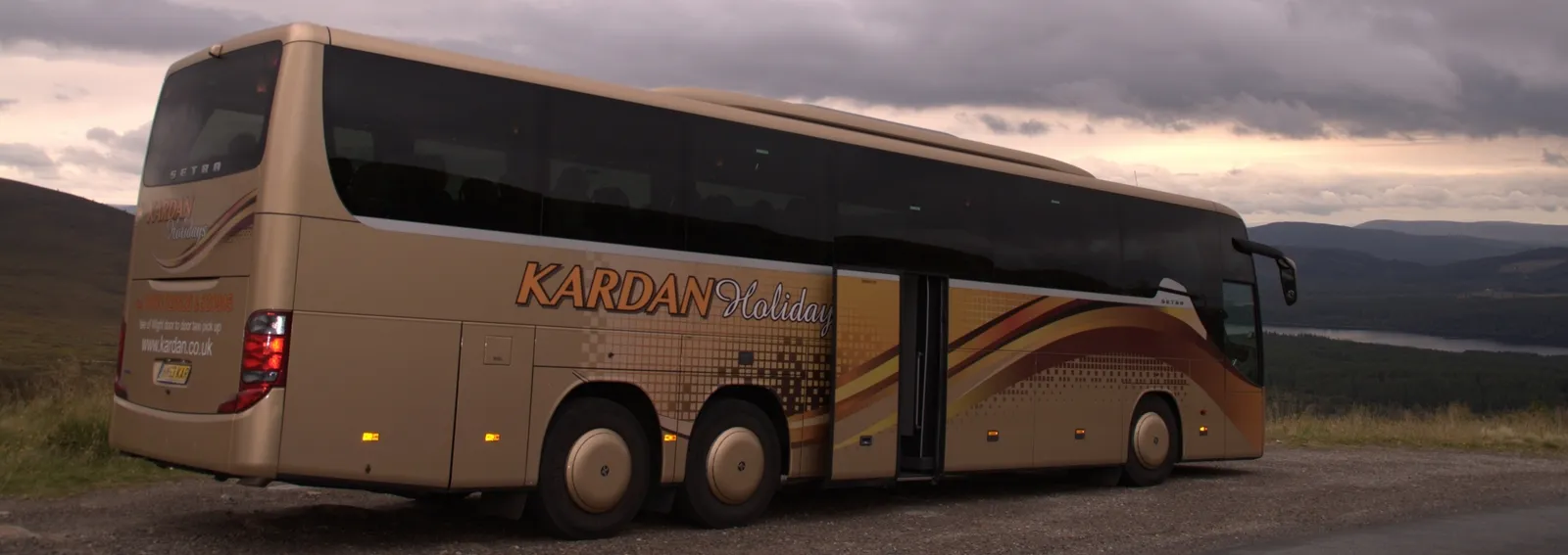 A Kardan Travel coach parked by a loch at dusk